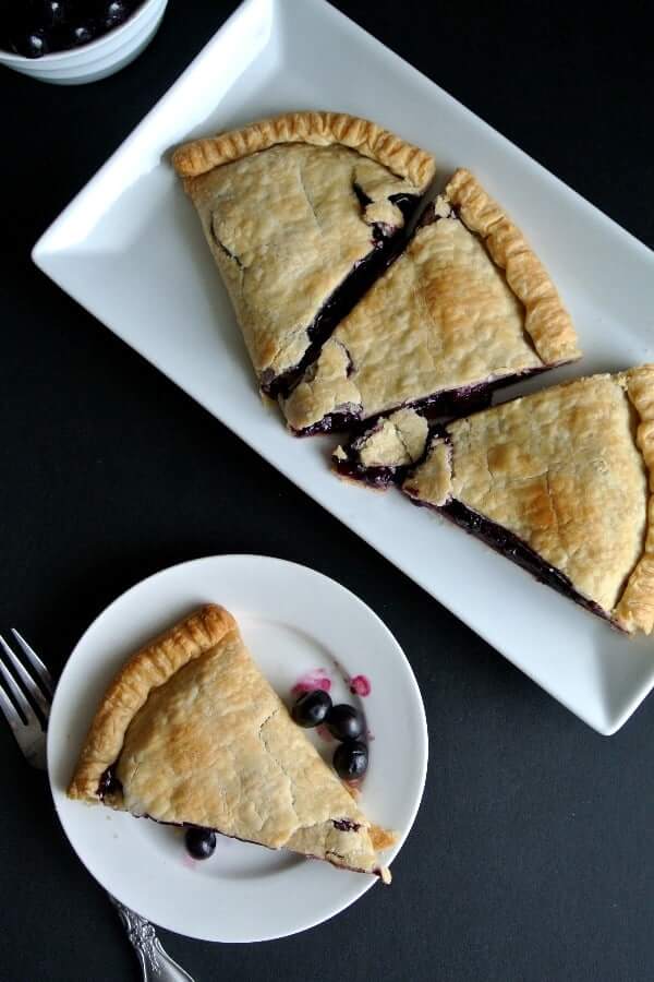 Overhead view of a baked pie with blueberries and sliced on a white plate.