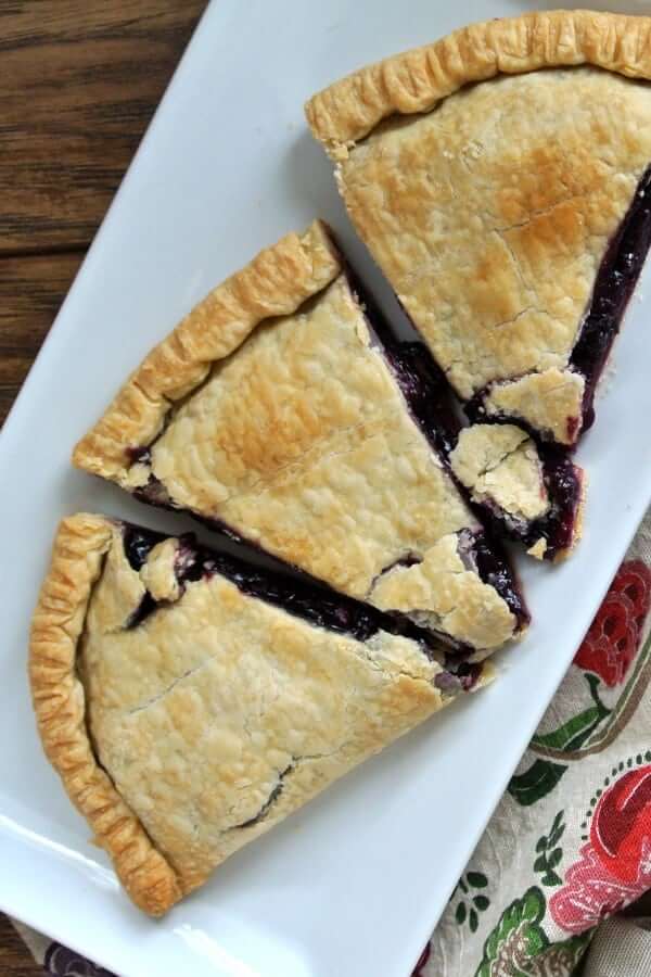 Overhead view of a baked half pie with blueberries and sliced on a white plate.