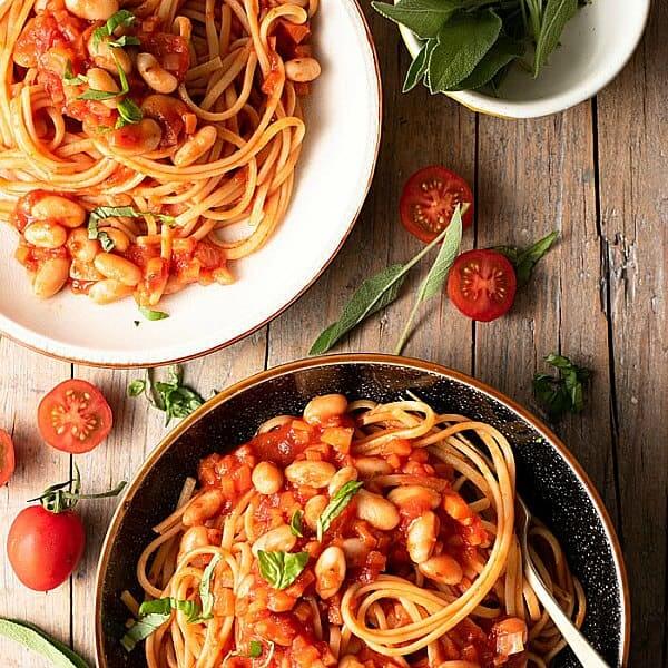 Overhead photo of two differently styled bowls filled with Tuscan pasta and beans and garnished with fresh herbs.