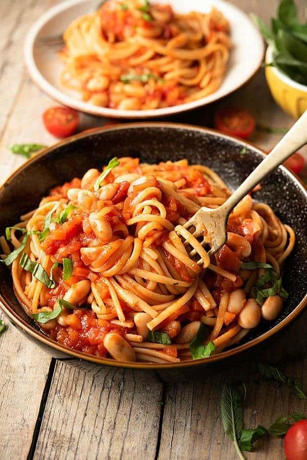 Pottery bowl is filled with pasta and beans and is being twirled on a fork.