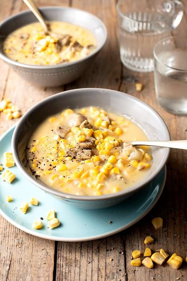 A tilted bowl full of soup with a spoon filled and ready to be lifted for a bite.