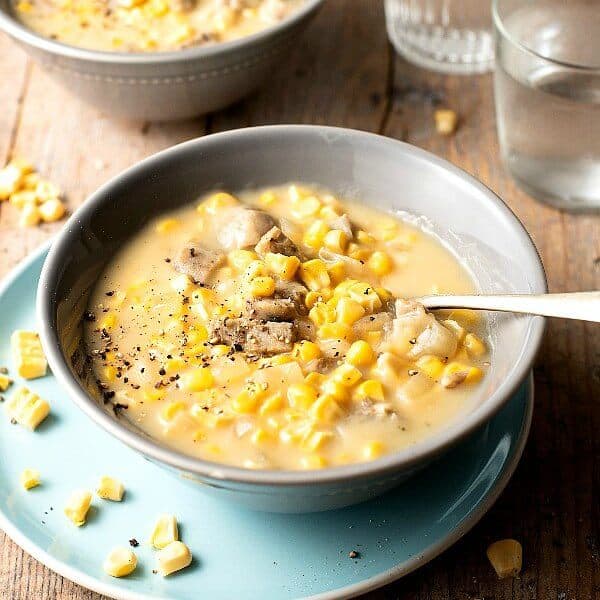 A Bowl filled with corn chowder with a spoonful sitting in the center waiting for a bite.