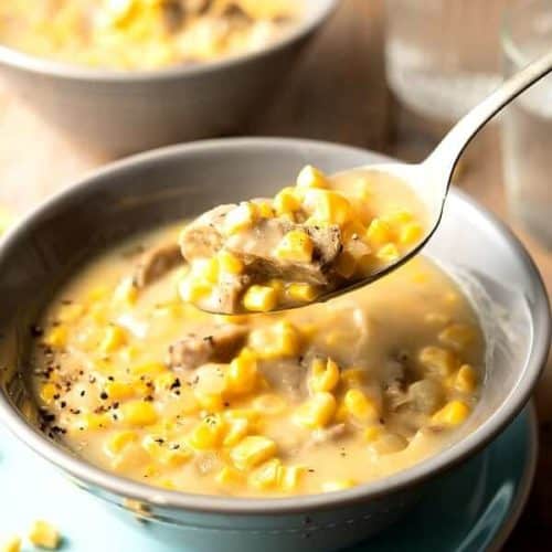 Close-up photo of a spoonful of corn chowder with chunks of meatless sausage and fresh corn kernels.