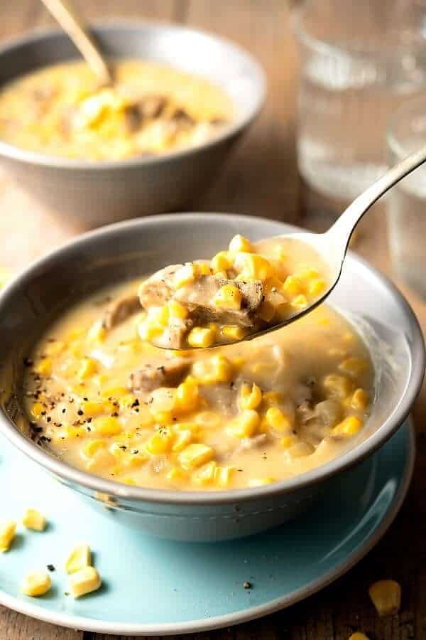 Close-up photo of a spoonful of corn chowder with chunks of meatless sausage and fresh corn kernels.