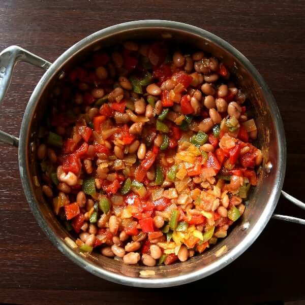 Overhead photo of a skillet filled with sauted and cooked mixed veggies along with pinto beans.