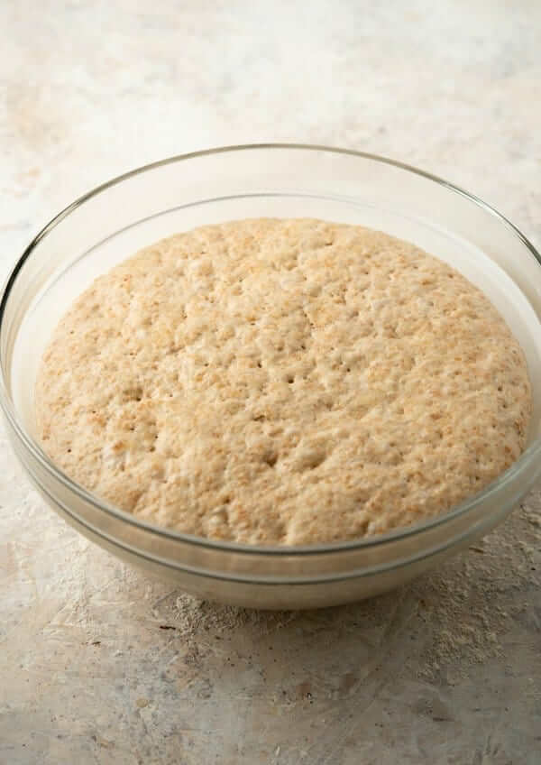A clear bowl is filled with a light and fluffy dough that has risen for it's first rise.