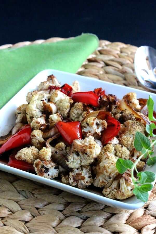 Andled view of roasted cauliflower and veggies caramelized on a square white plate.