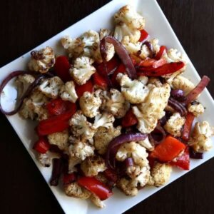 Overhead view of roasted cauliflower and veggies caramelized on a square white plate.