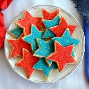 Star shaped Shortbread Cookies in the colors of red and blue and are piled on a plate and are photographed from above.
