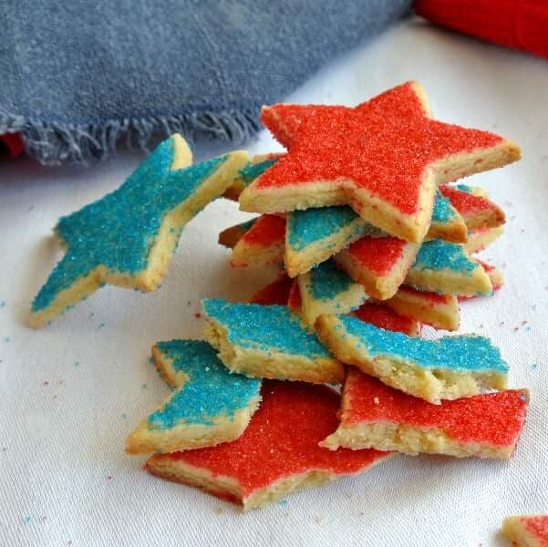 Star shaped Shortbread Cookies in the colors of red and blue and are piled on a cloth napkin and angled every which way.