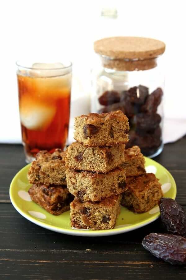 Stack and pile of banana bread infront of a glass of iced tea and a jar of dates.