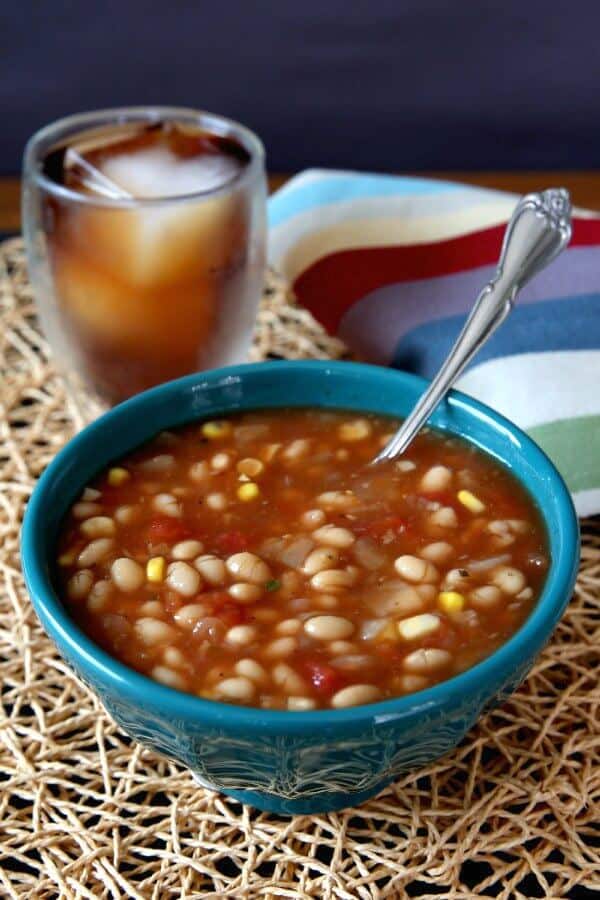 Navy Bean Soup in a turquoise bowl with a spoon laying inside and iced tea over ice behind.