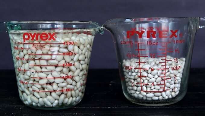 Two measuring cups showing dried white beans and soaked white beans.