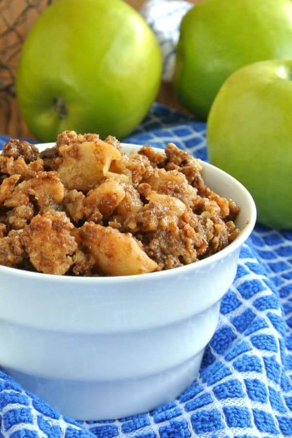 Golden Apple Crumble is in a white bowl and sitting on a blue and white checkered cloth with the bowl cropped in half for the photo.