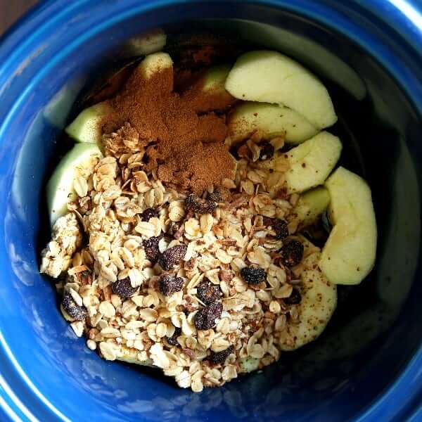 Overhead view of all ingredients added to a blue interior crockpot including apples and oats.