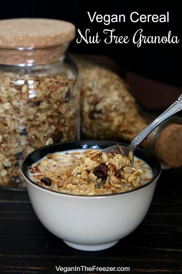A bowl full of granola is being scooped up for a bite. With two jars of homemade cereal behind.