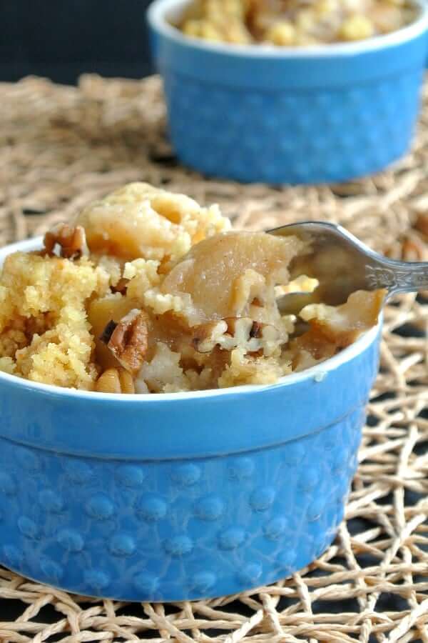 Cropped photo of a blue bowl filled with golden apple pie cake and being forked up for a bite.