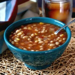 Navy Bean Soup in a turquoise bowl sitting on an ivory woven mat with a spoon inside the soup.
