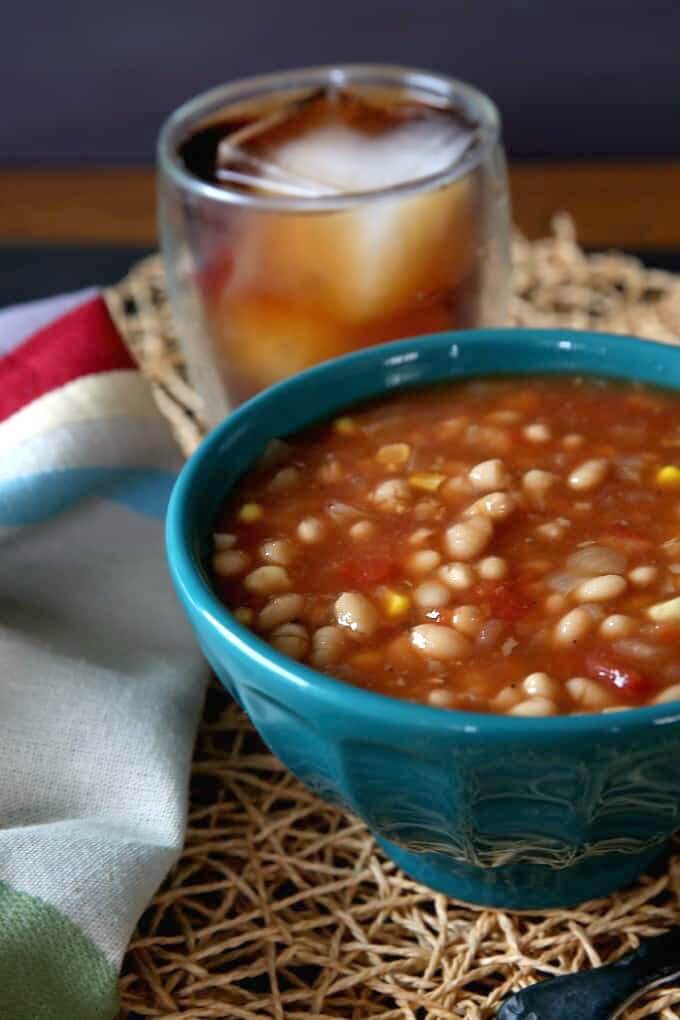 Turquoise bowl filled with rich brothed navy bean soup and the bowl is cropped in half for the photo.