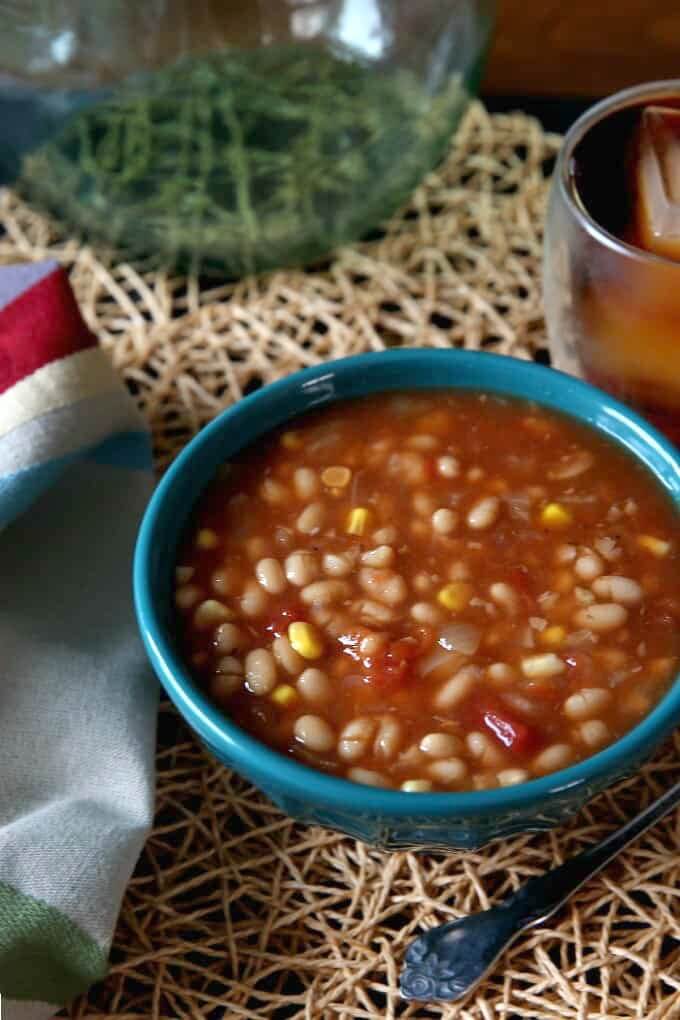 Navy Bean Soup in a turquoise bowl sitting on an ivory woven mat with a spoon on the side.