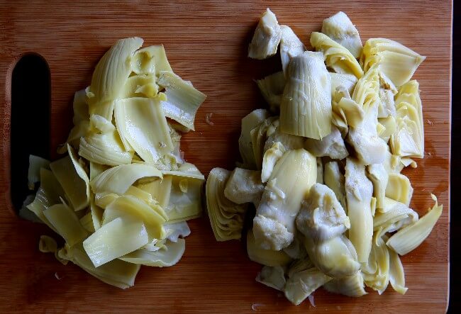 Overhead photo os quartered artichoke hearts on one side and discarded tough leaves on the other.