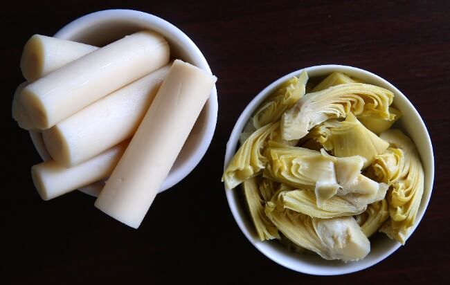 Overhead view of Hearts of palm in a small white bowl and artichoke hearts in the other.
