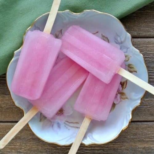 Overhead view of four pink popsicles on an antiqued flower dish and then on a wooden picnic table.