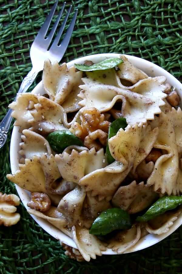 Over head view of a serving bowl full of bowtie pasta on a green mat.