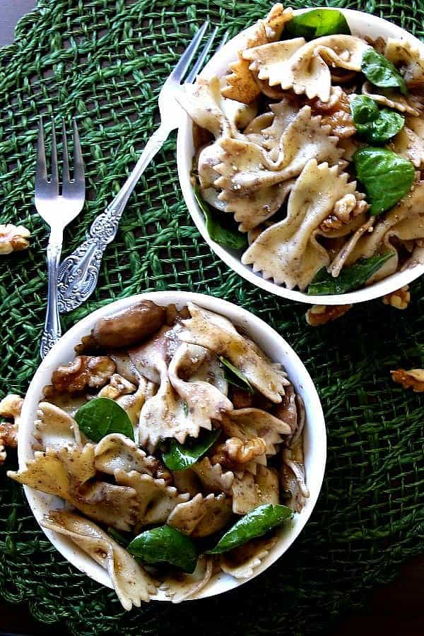 Overhead view of two bowls of pasta salad showing greens of spinach and browns of walnuts.