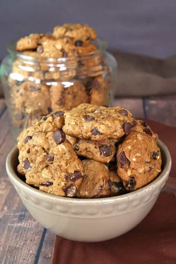 Bowl full of a couple dozen cookies with a full glass cookie jar behind.