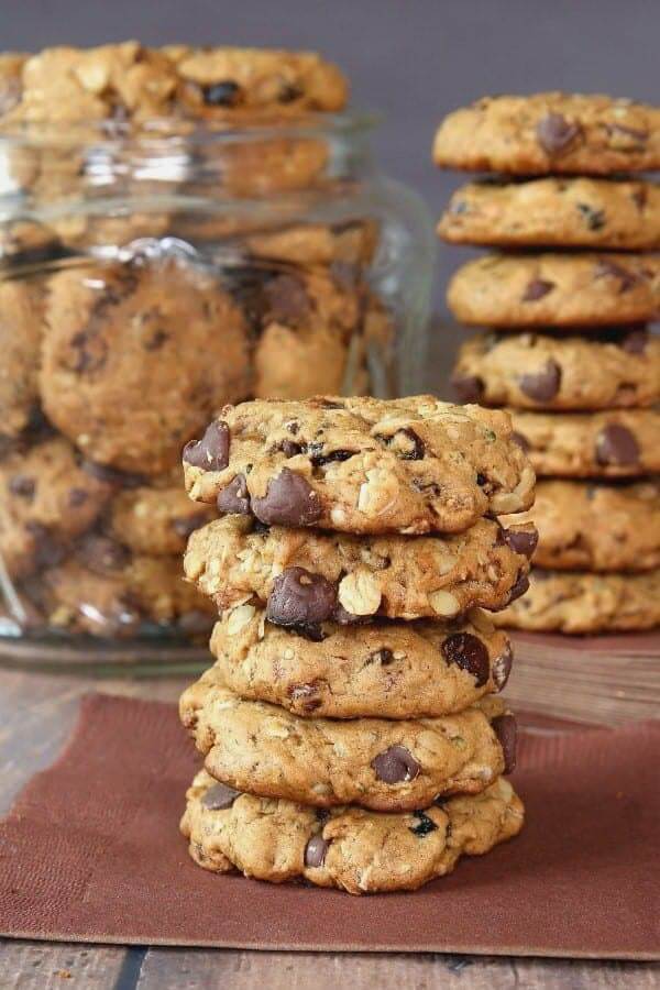 Five cookies are stacked high on a brown napkin with more cookies stacked behind.