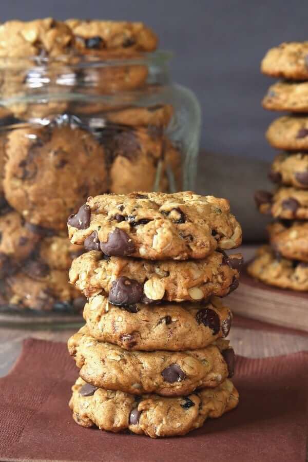 Five cookies stacked on a chocolate napkin with more cookies behind in a glass jar.