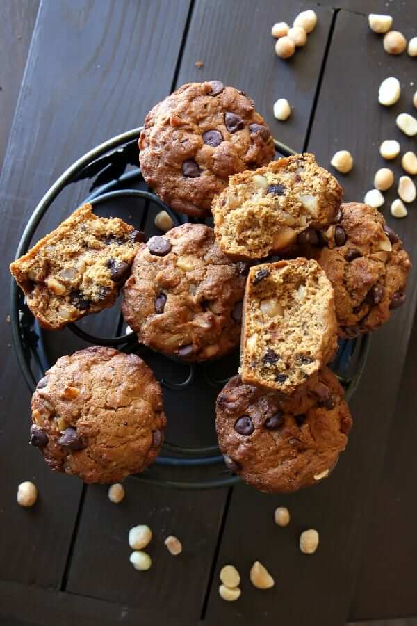 Overhead view of vegan muffins chocolate chip and macadamia nut filled, with some broke in half on top of an iron trivet.