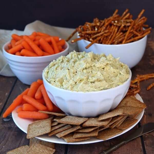 Square photo of a bowlful of creamy dip surrounded by pretzels, chips and carrots.