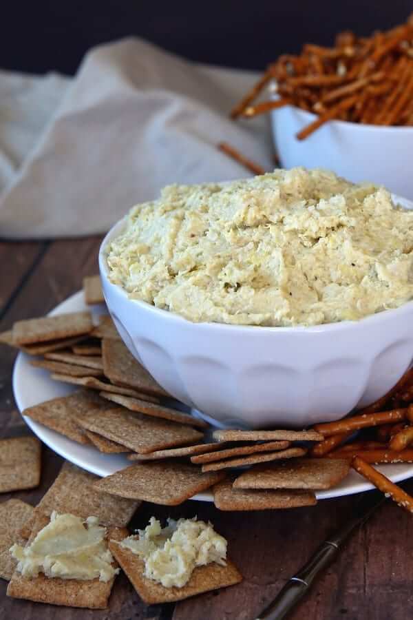 Cropped white bowl filled with a creamy spread with wheat thins around the plate.