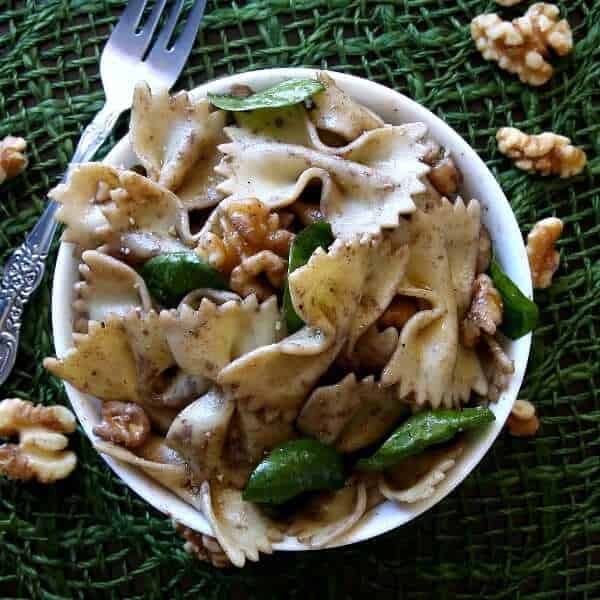 Overhead view of a white bowl with one serving of Mediterranean pasta salad showing spinach and walnuts.