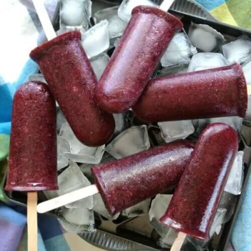 Overhead view and close-up of deep purple blueberry popsicles on a bed of ice.