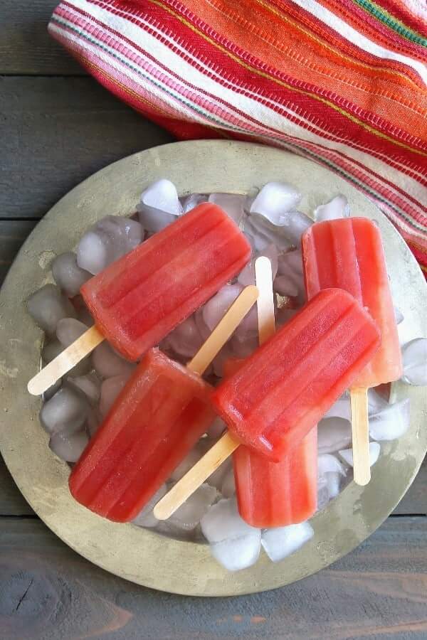 Overhead photo of coral colored popsicles on ice and a silver platter.