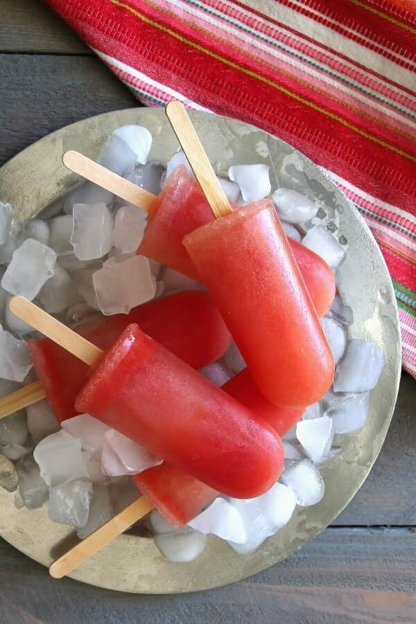 Overhead photo of round coral colored popsicles on ice and a silver platter.