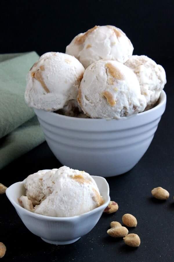 A white bowl with 5 huge scoops of ice cream with one single scoop and bowl in front.