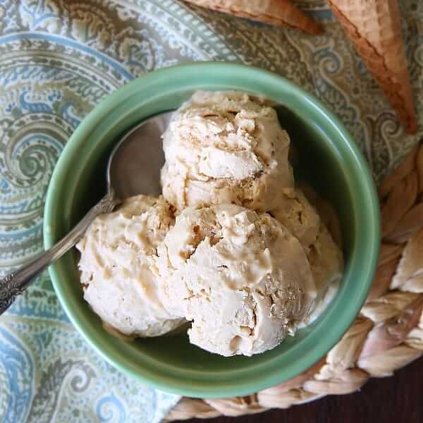 Overhead view of a green bowl full of Cookie Butter Ice Cream on a straw mat.