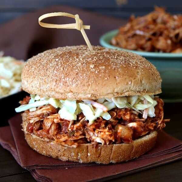 Front view of a fat sandwich on a bun with coleslaw and a bowl of more BBQ jackfruit behind.
