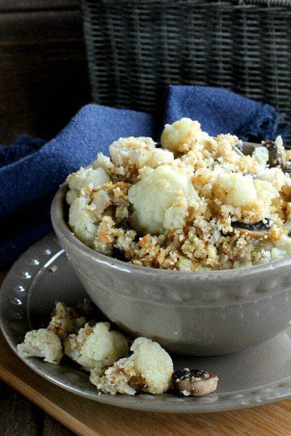 Cropped beige bowl overflowing with vegan cauliflower casserole and a navy cloth napkin.