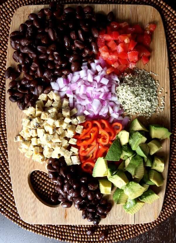 Overhead view of a wood cutting board loaded seven different chopped veggies.