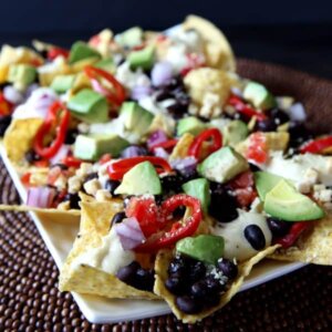 Front angle view of veggie loaded nachos on a white rectangle plate.
