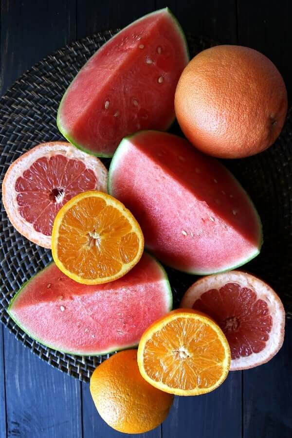 Overhead view of fresh watermelon and citrus cut open on a straw background.