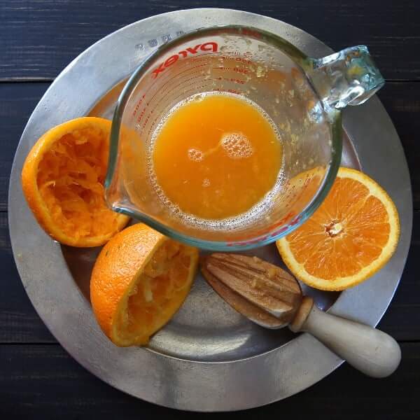 Overhead view of a reamer next to squeezed oranges with their juice in a measuring cup.