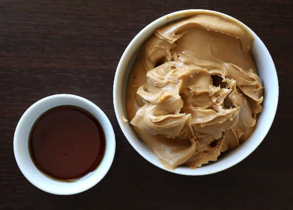 Above photo of a a small bowl of creamy peanut butter and maple syrup.