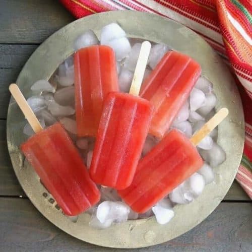 Overhead photo of bright coral colored popsicles on ice and a silver platter.