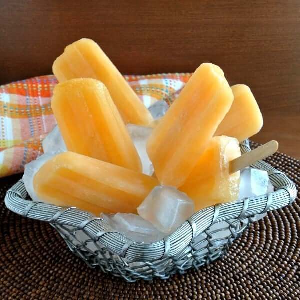 Tilted silver metal basket holding ice and real fruit popsicles.